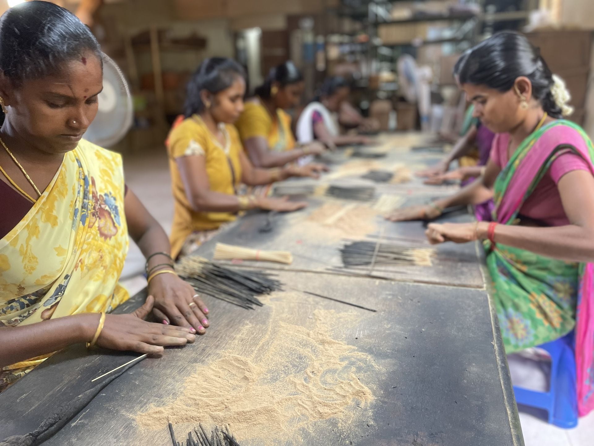 Women of the PremaNature workshop rolling incense sticks by hand along a long wooden table